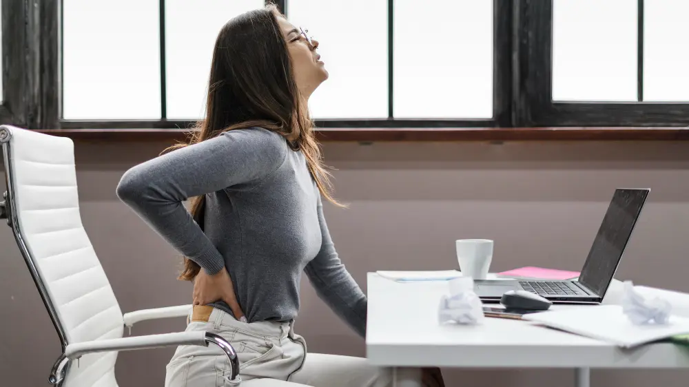 Woman sitting at desk working on laptop while experiencing herniated disc back pain