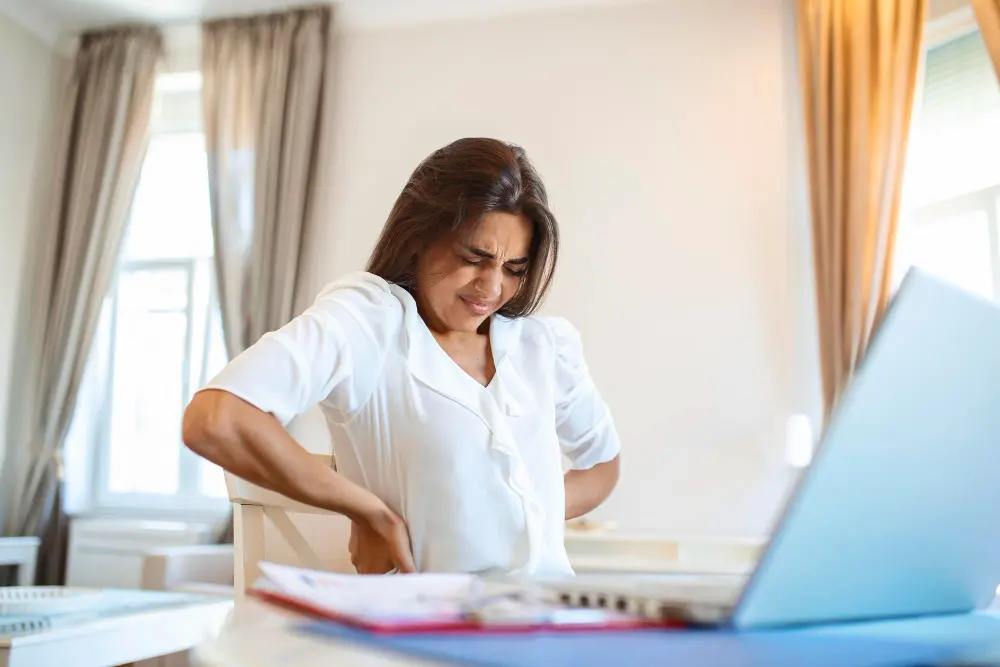 Woman using laptop while suffering from severe herniated disc pain in lower back