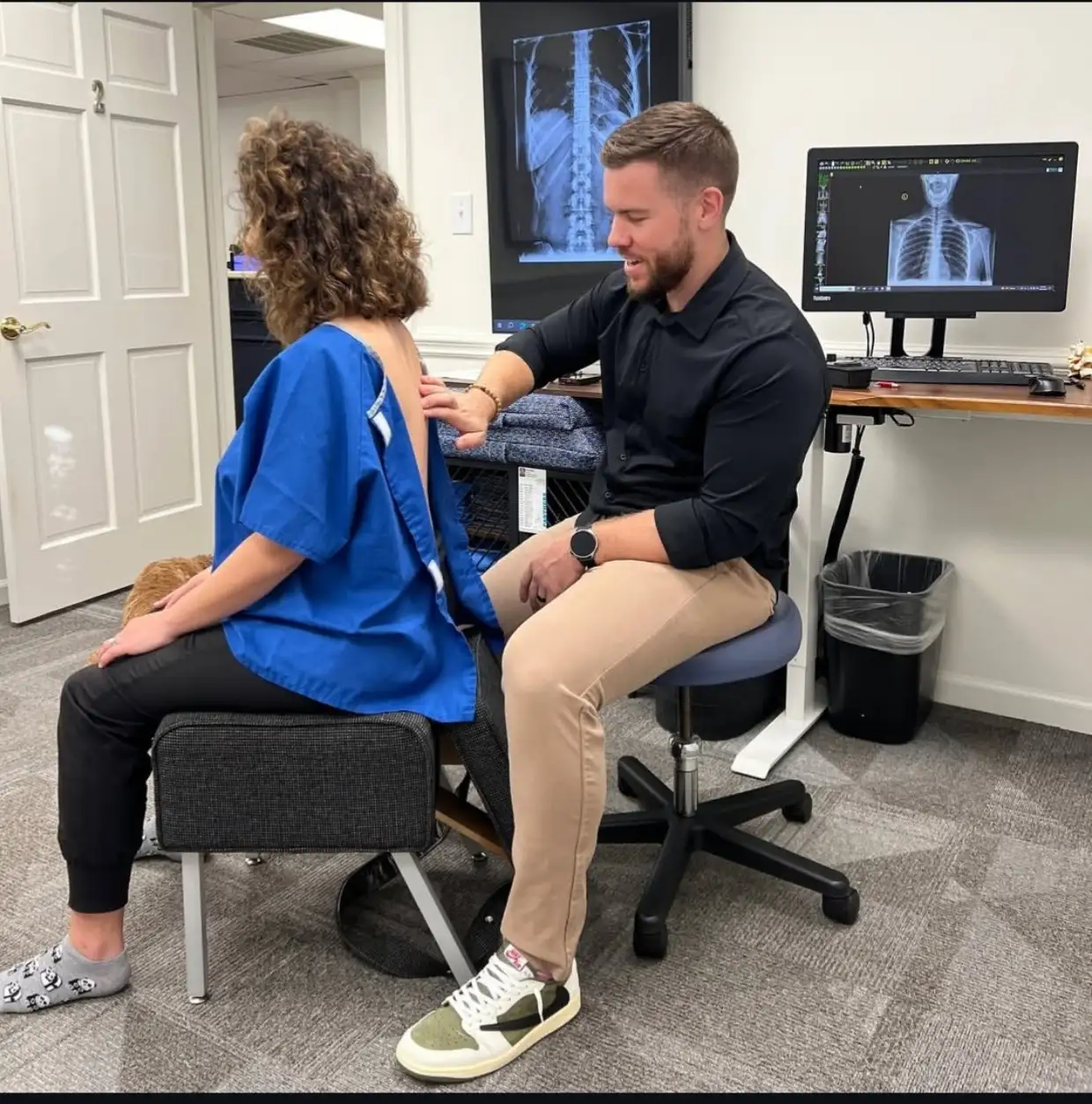Chiropractor assessing upper back alignment while reviewing digital spine X-rays at Axiom Chiropractic in Charlotte NC
