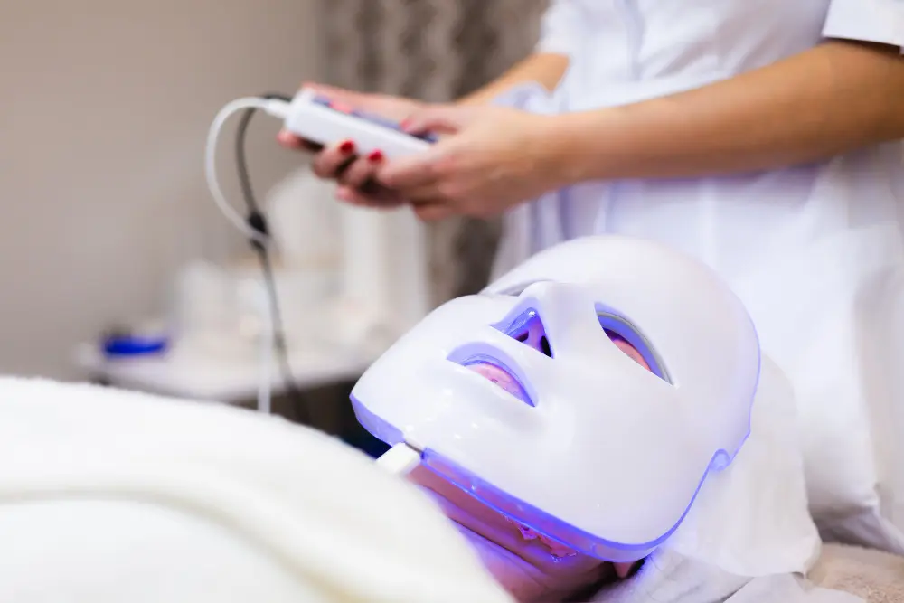 Chiropractor using red light therapy device on female patient’s face