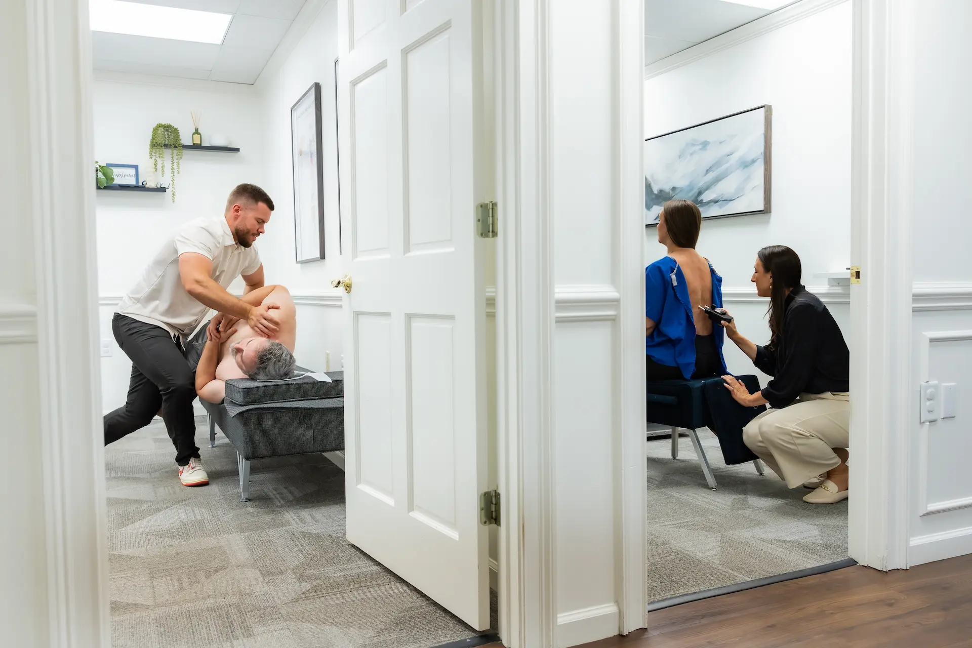 Two practitioners treating patients in separate rooms of a clinic. One practitioner adjusts a male patient's back, while another uses a device on a female patient's back.